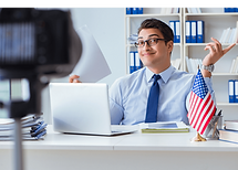 A man working behind a desk with a laptop and a US flag
