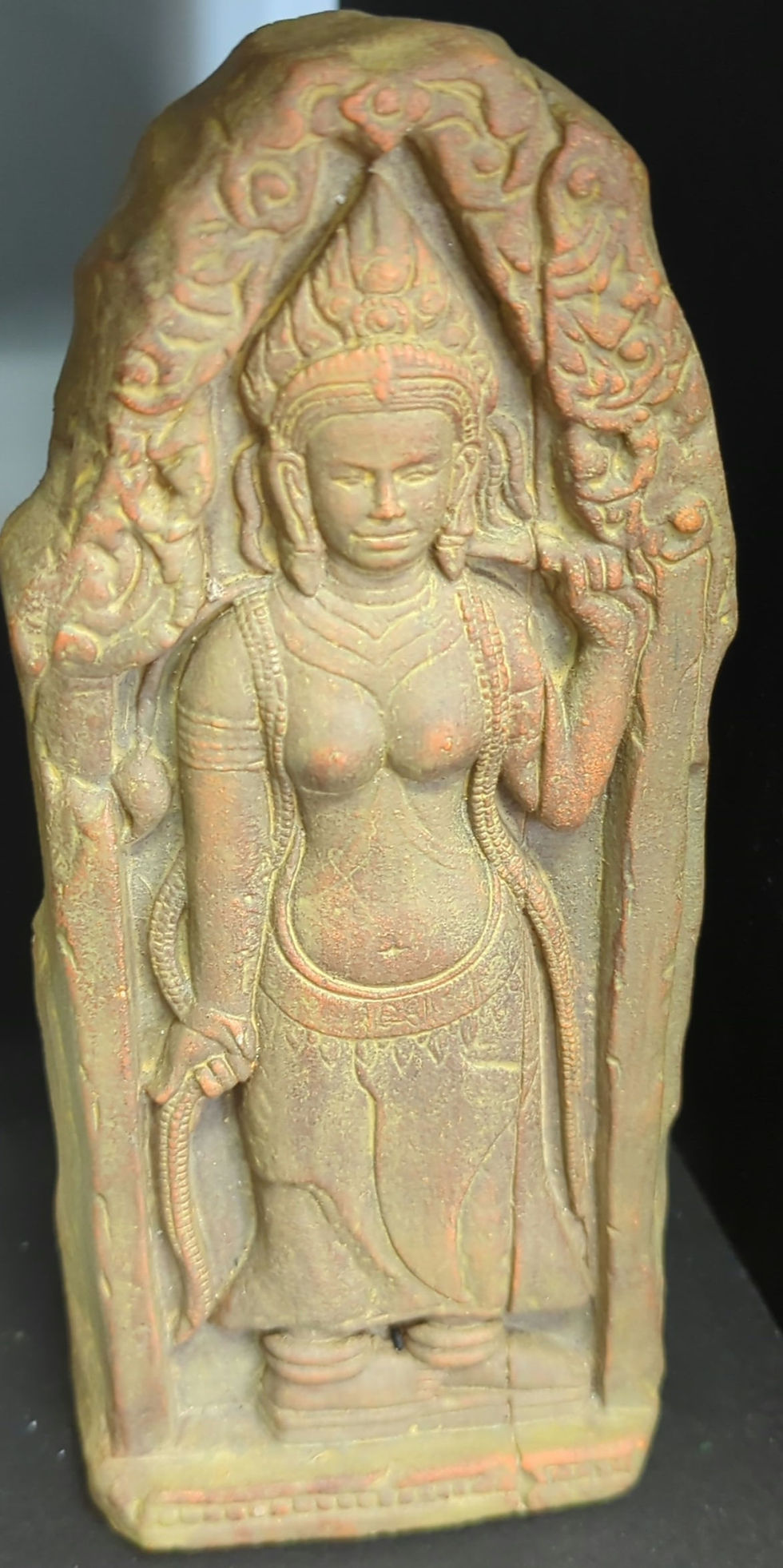 Ancient stone statue of a serene woman in traditional attire, with intricate carvings and muted earthy tones, against a dark background.