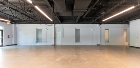 Empty multipurpose room at Lighthouse School before acoustical treatment, showing bare painted brick walls, cement floors, and open metal ceiling