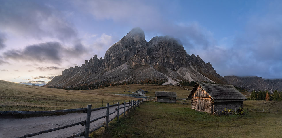 Sunrise at Passo delle Erbe in the Dolomites with meadow, mountain huts, and the peak of Sass de Putia under a purple sky