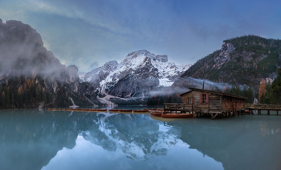 Lago di Braies in the Dolomites before sunrise with boat house, wooden boats, mist, and reflections on the lake