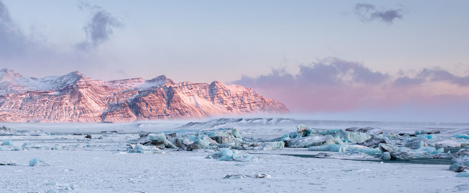 Scena invernale ghiacciata a Jökulsárlón, con la luce del tramonto che illumina il ghiaccio e le montagne sullo sfondo.