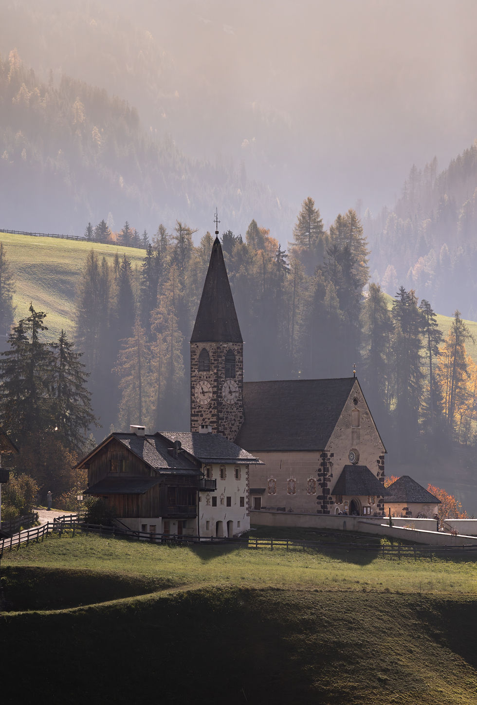 The church at Santa Maddalena in the Dolomites against a hillside covered by autumn trees.