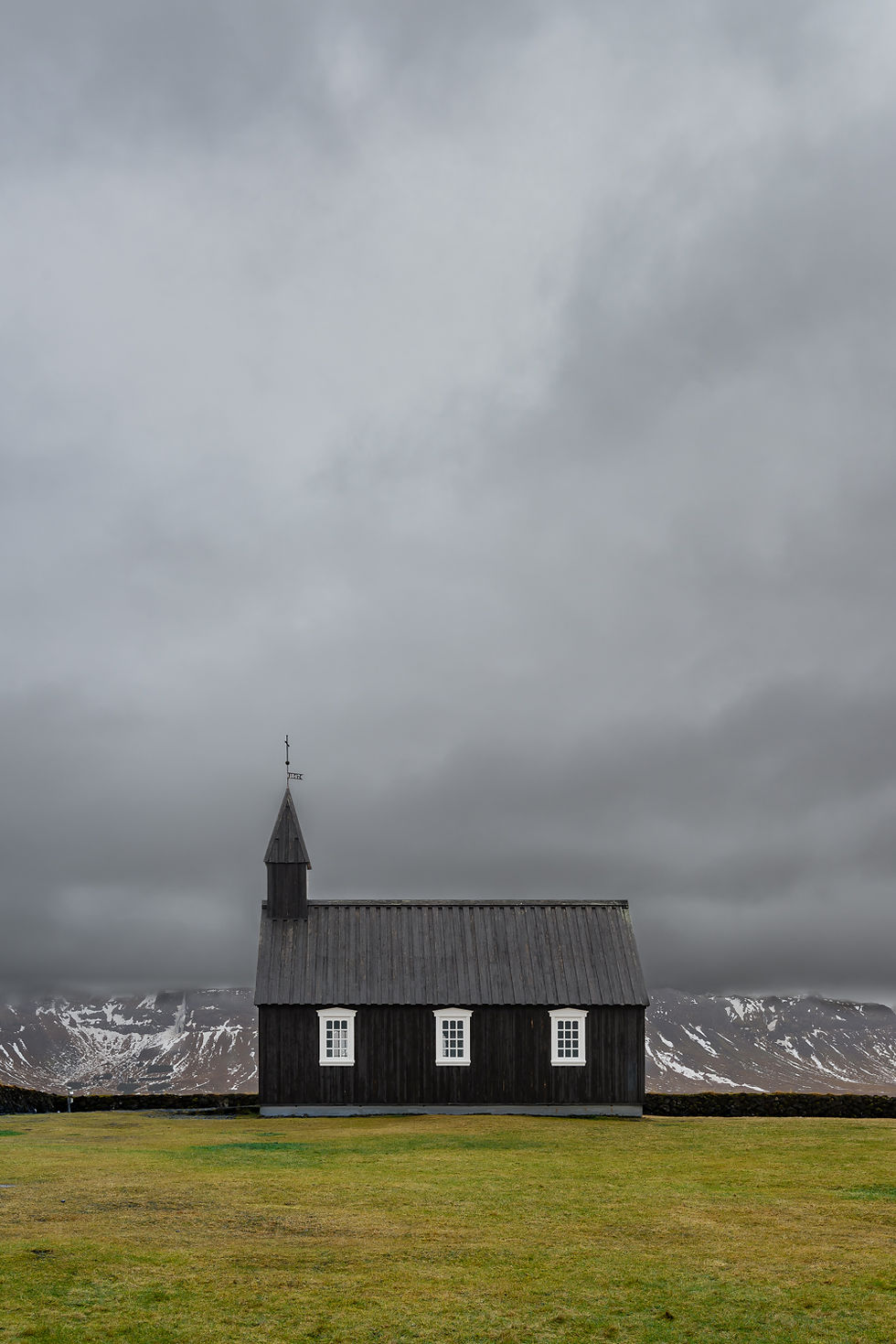 The black church Búðakirkja under a grey cloudy sky with green and yellow grass in the foreground
