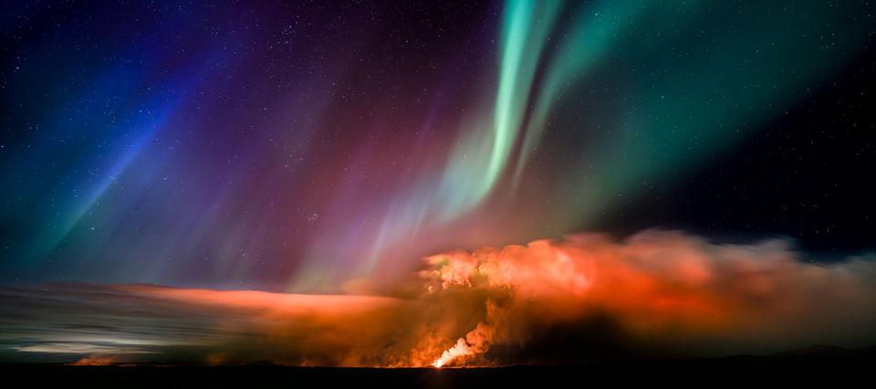 L’aurora boreale appare sopra la colonna vulcanica a Geldingadalir, fondendo lava e luci del nord in un solo scatto.