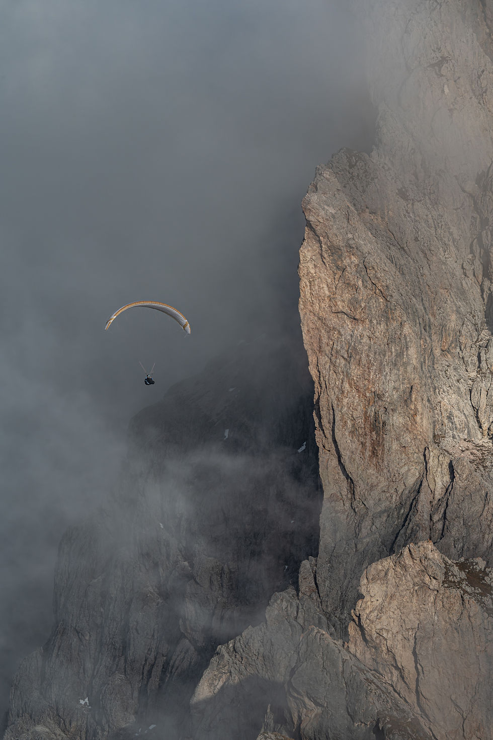 A paraglider moving through mist next to towering rocks at Seceda Ridge in the Dolomites