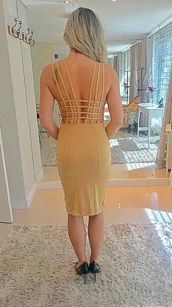 mulher loira com vestido na cor bege. Ao fundo um ateliê de costura.