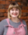 Marketing Coordinator Emily has a blonde bob, and is wearing pink lipstick. She's wearing pink dungarees with a black and white stripey top.