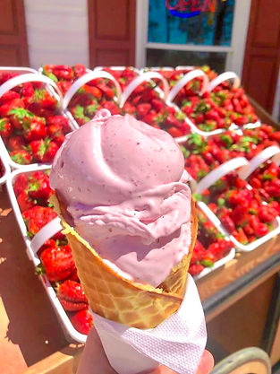 Closeup of a strawberry ice cream cone with baskets of strawberries in the background