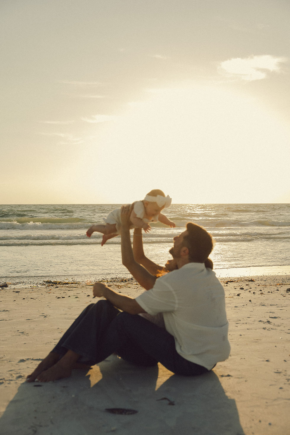 Man lifting baby on beach at sunset