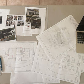 An image of architectural and design plans for the "Sunny Spacious Forever Home" laid out on a table.