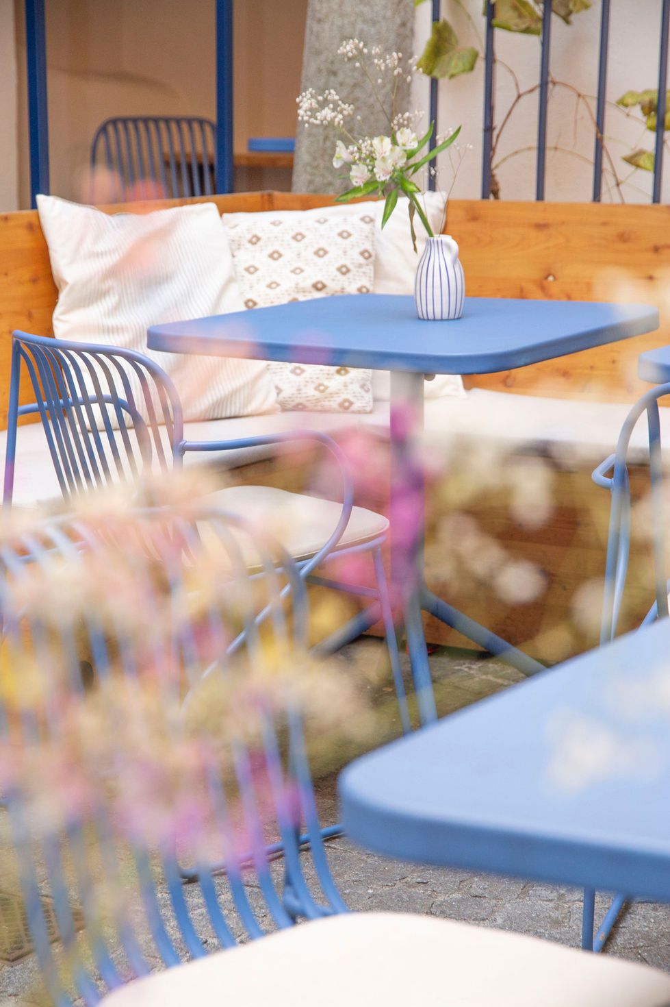 Holzbank und blaue Garnituren in modern eingerichtetem Gastgarten mit hübschen pflanzenschmuck
