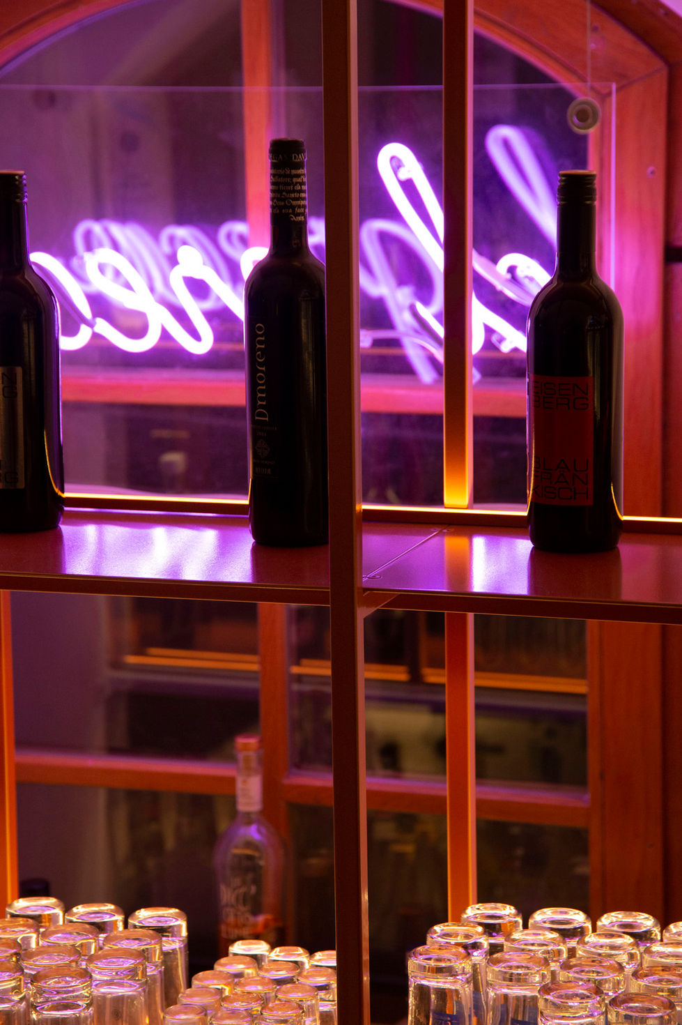 Detailaufnahme eines Weinregals in einer bar mit Leuchtschrift im Hintergrund