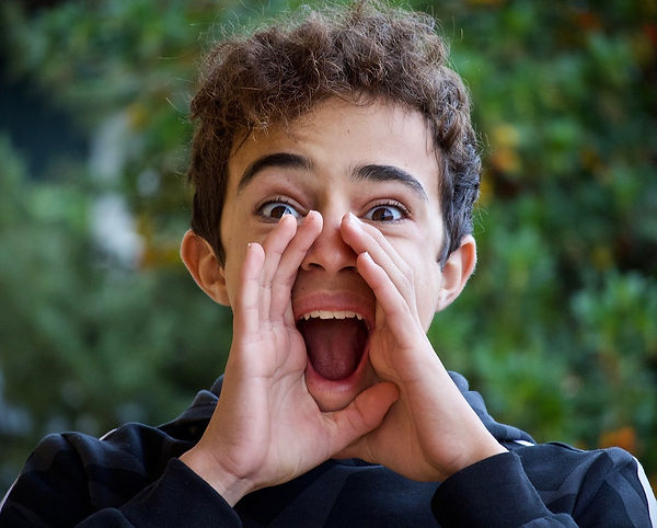 A brown haired teenage boy shouting with hands cupped around his mouth, representing taking quotes out of context and spreading misinformation online. Trees are faded in the background.