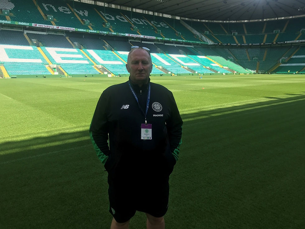 A person stands on a sunny football field, wearing black sports attire. "NEW BALANCE" and "MAGNERS" logos visible. Rows of green seats in the background.
