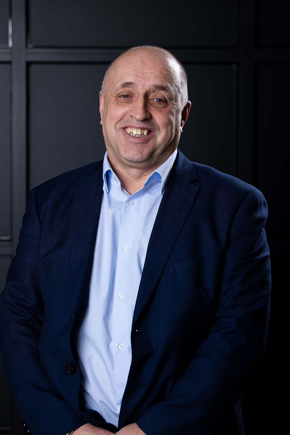 Eddie Rutherford in a blue suit smiles warmly against a dark, paneled background, conveying a professional and approachable mood.