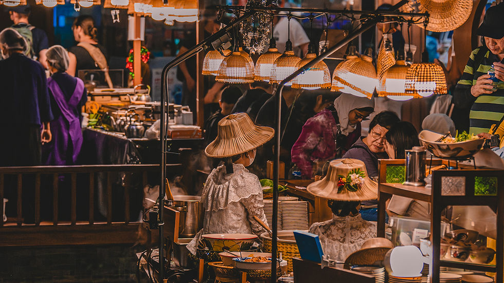 Warm lit floating market with vendors wearing conical hats, selling food, and shoppers moving through a busy, colorful setting.