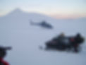 A helicopter is sitting on the ground on a snowy mountain. In the foreground is an unmanned snowmobile.