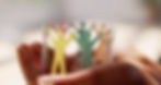 Close-up of a circular chain of colorful paper cut-out figures holding hands. The figures are standing upright on a surface, symbolizing unity and diversity. The focus is on the front figures, with others slightly blurred in the background.
