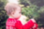 Baby in a red top putting on a red bauble onto a Christmas tree