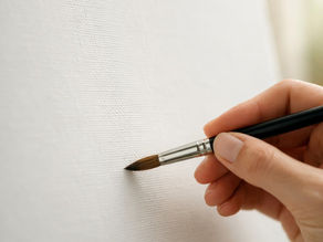 Paintbrush gently touching a blank white canvas, capturing that quiet, powerful moment when creation begins.