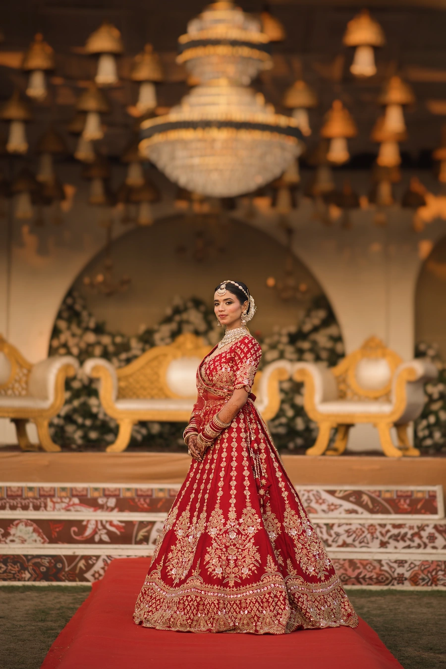 Indian bride in red lehenga posing on a decorated wedding stage with elegant lighting