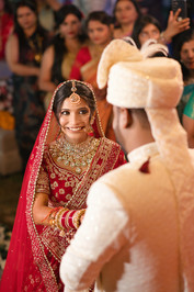 Joyful bride looking at groom during varmala at Hyatt Regency, Dehradun, surrounded by cheering guests.