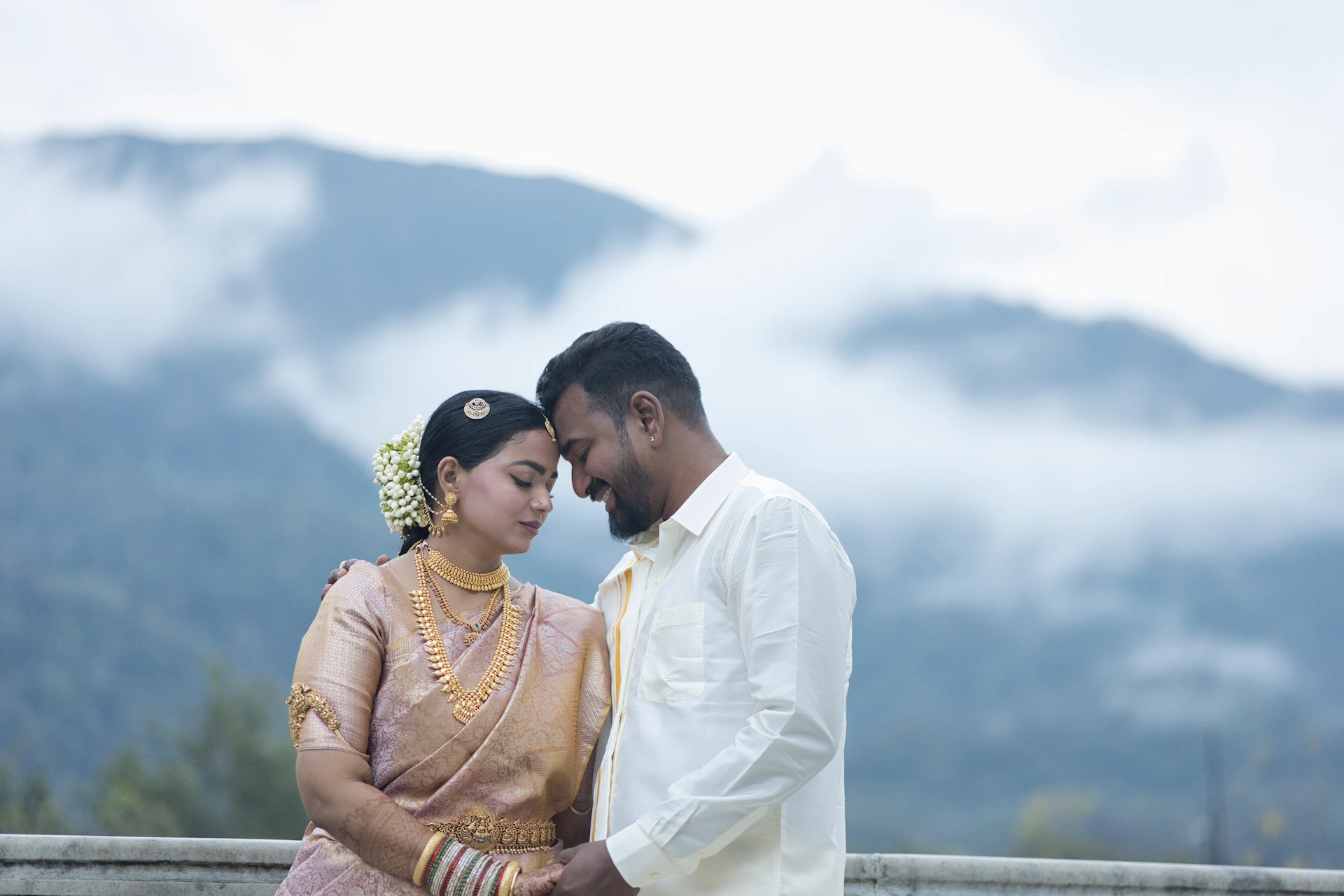 Romantic pre wedding couple in Rishikesh sharing an intimate candid moment with misty mountain background, bride in traditional silk saree and groom in white attire, Uttarakhand destination wedding photography