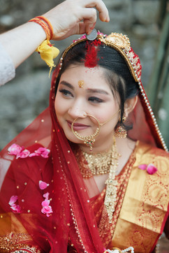 Smiling bride in red veil, gold jewelry, traditional Indian wedding ceremony.