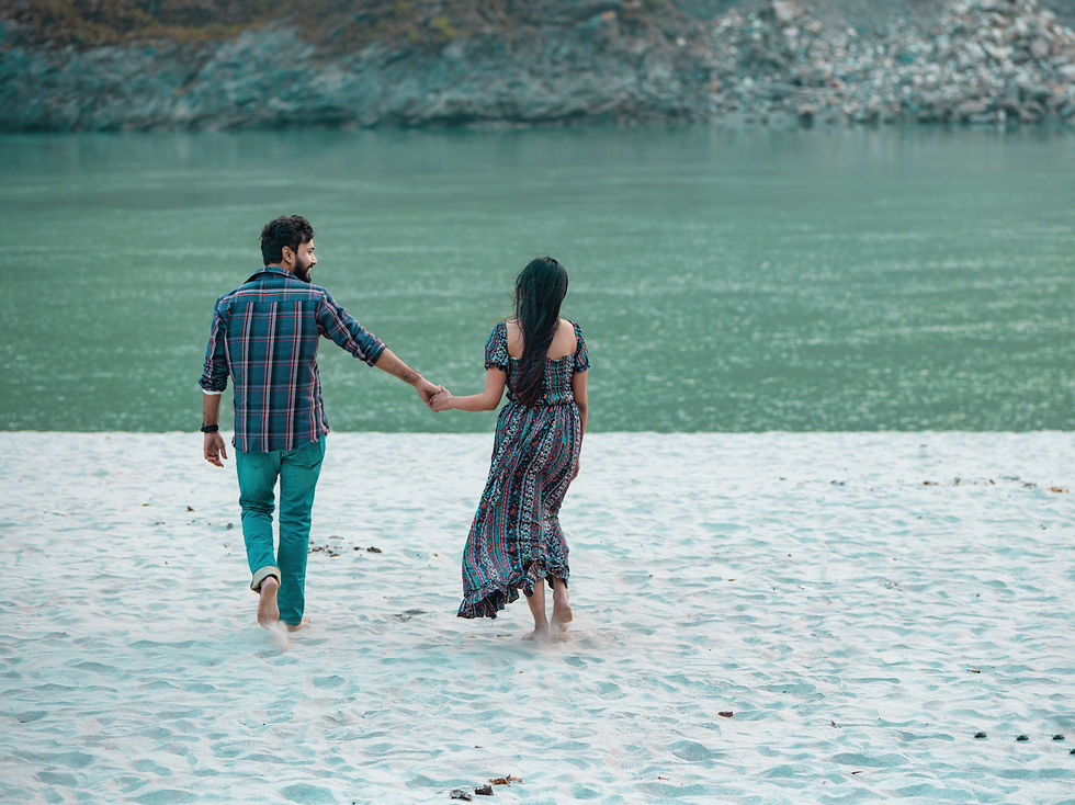Romantic pre-wedding photoshoot of a couple standing on the banks of the Ganga River in Rishikesh, with flowing water, lush greenery, and the iconic Himalayan foothills in the background.