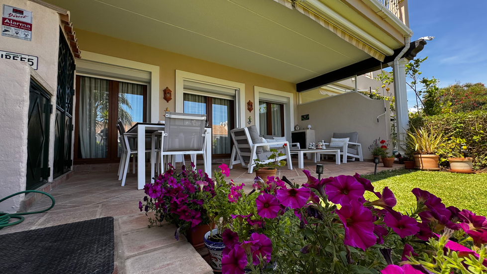 White patio furniture with vibrant pink flowers nearby.