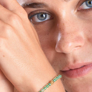 Woman with striking blue eyes wearing a delicate green beaded bracelet.