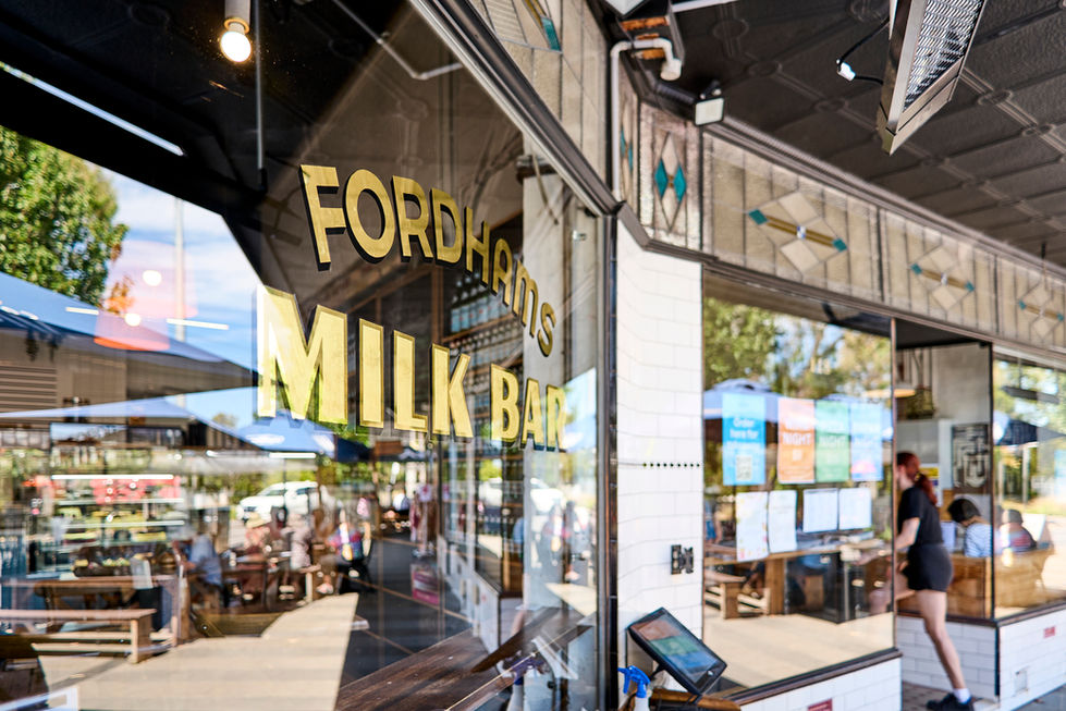 Patio area of a milk bar with patrons enjoying their meals and conversations under umbrellas.