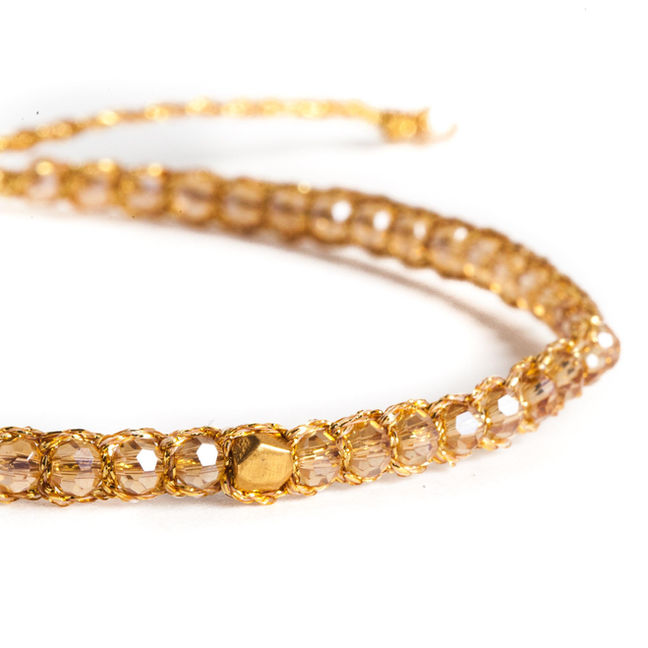 Gold beaded necklace closeup with faceted clear beads on white background.