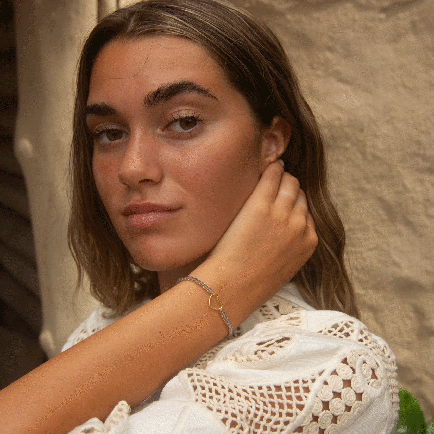 Young woman wearing a gold heart charm bracelet and white lace top.