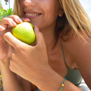 Smiling woman holds a crisp green apple, enjoying the outdoors.