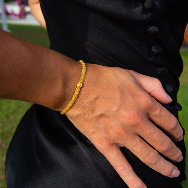 Woman's hand wearing a gold beaded bracelet with a sleek black dress.