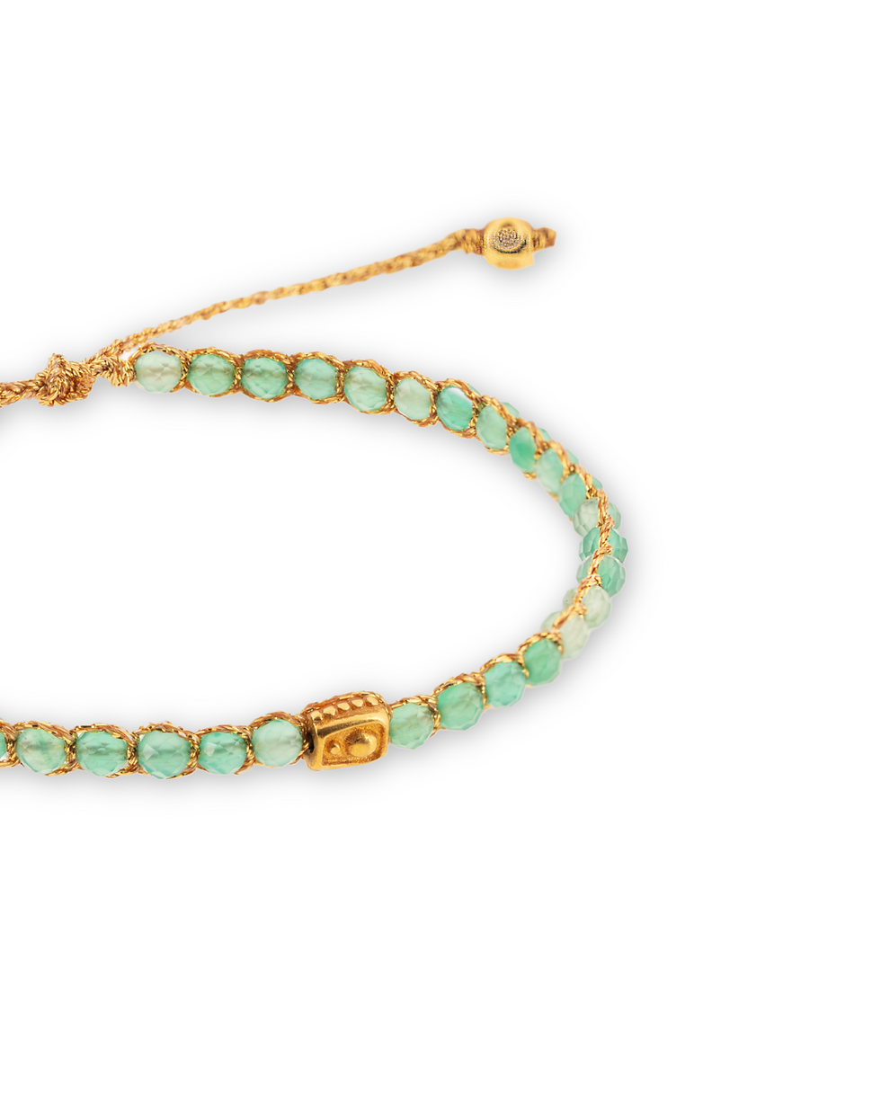 Bracelet with small green beads, golden cord, and decorative charm.