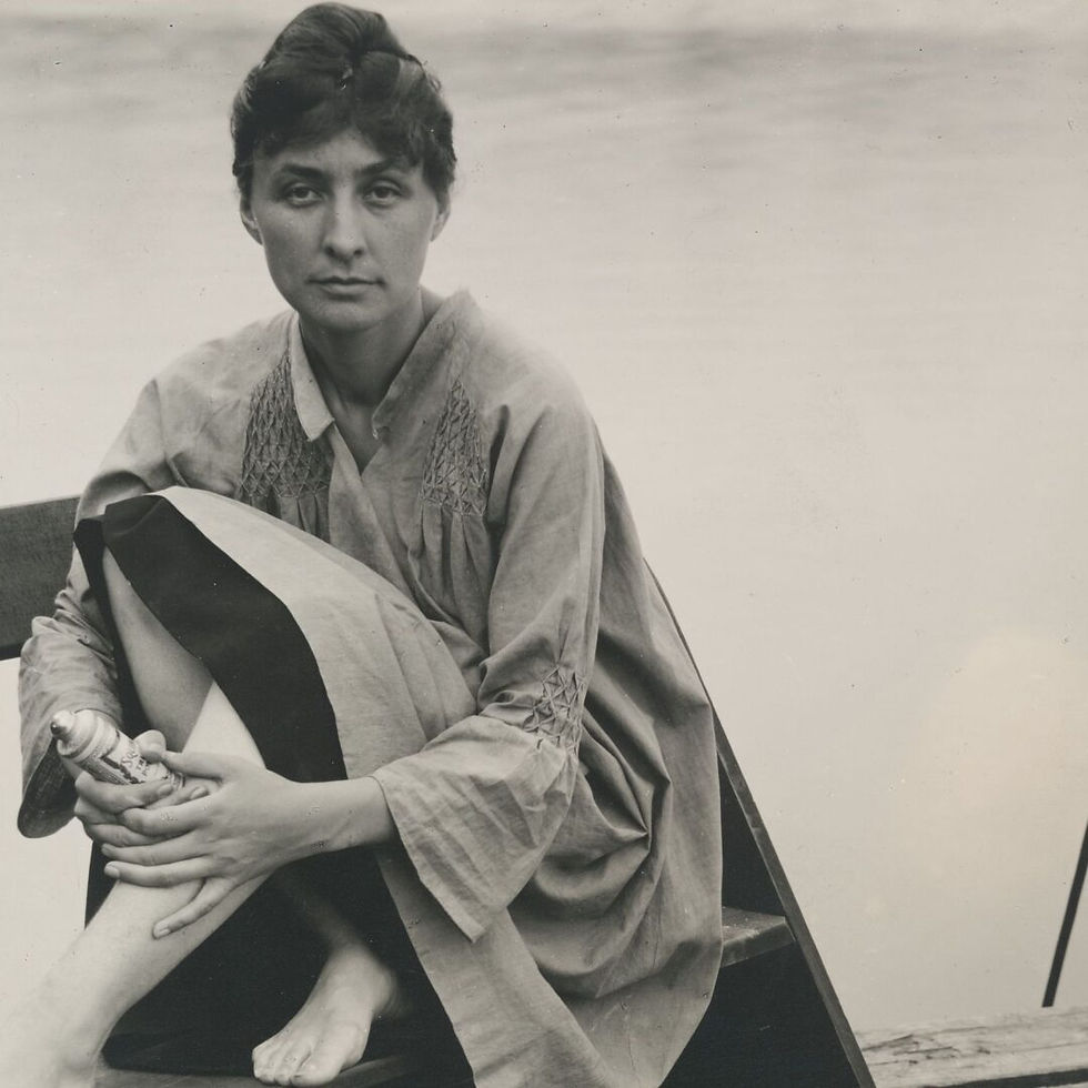 Black-and-white portrait of a serious woman sitting with a striped cloth on her lap, holding a spray can against a plain backdrop.