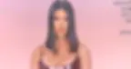 Kourtney Kardashian with straight black hair poses against a soft pink background, wearing a shiny dark top. Camera settings text overlays the image.
