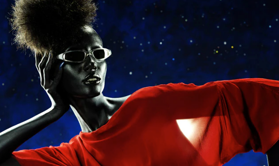 A person wearing glasses and a red garment poses against a starry night background. Their skin glows silver, creating a futuristic vibe. Image courtesy of Selima Optique.