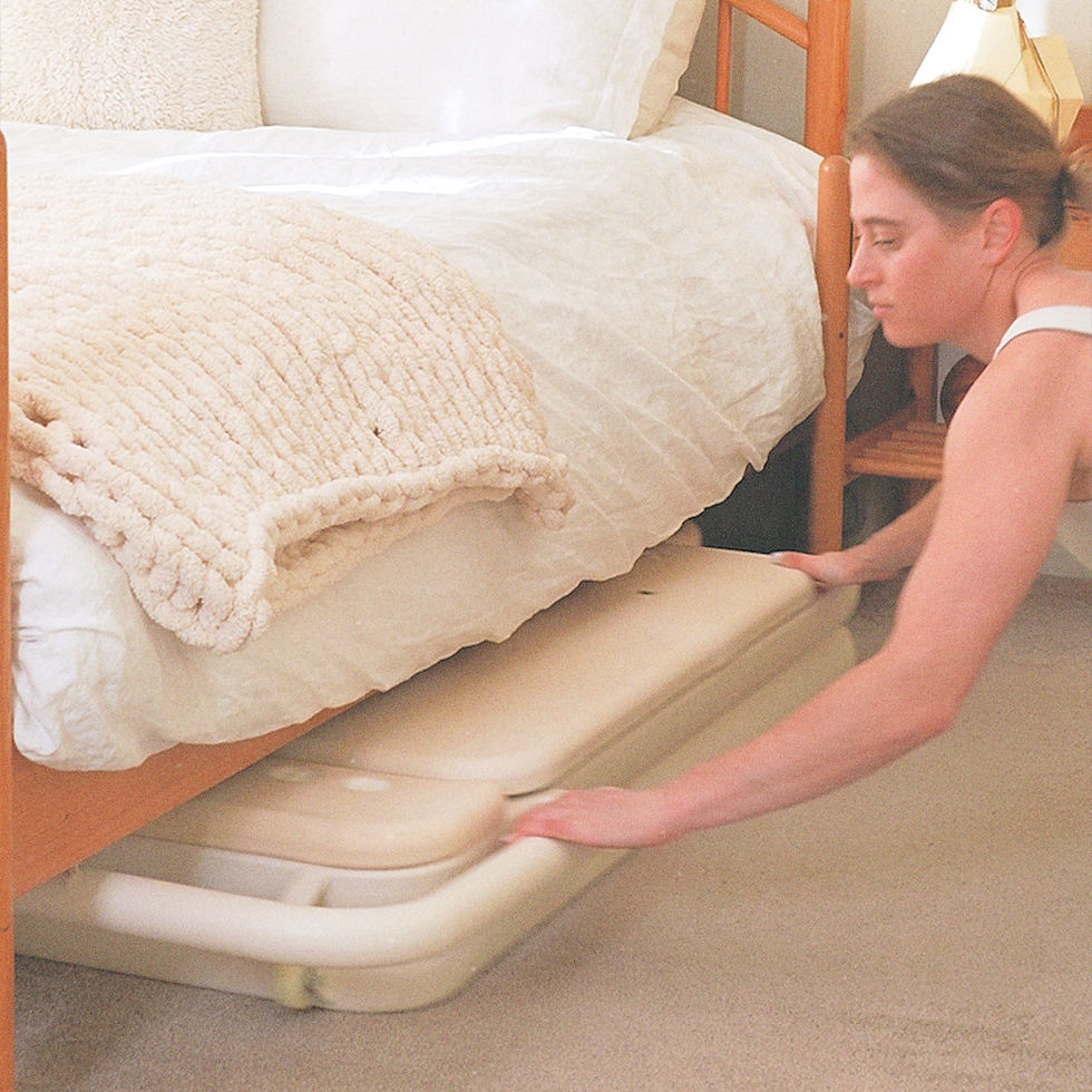 Person in a white shirt is pulling a beige board from under a bed with white bedding. Soft lighting creates a calm, organized ambiance.