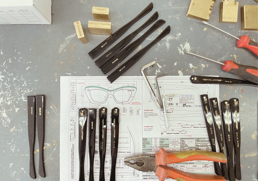 Glasses temple arms on design blueprints, surrounded by tools and screws on a gray table, evoke a precise and organized workspace.