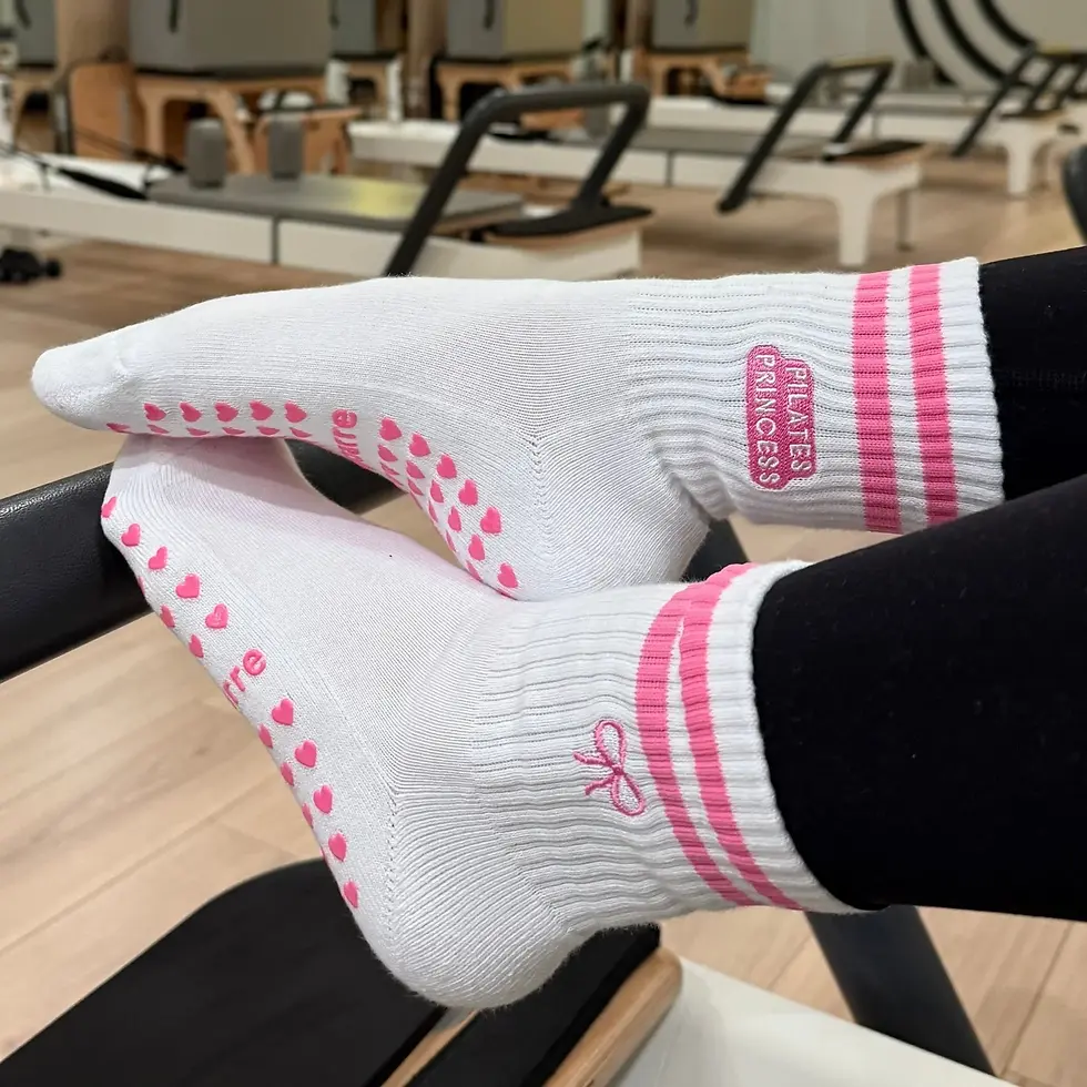 White socks with pink polka dots and "Pilates Princess" text, worn by someone on a Pilates reformer in a fitness studio.