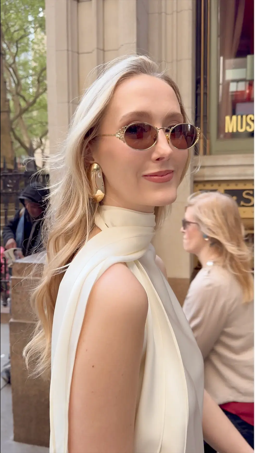 Ashlyn Lawrence, Designer behind fashion brand Centre Piece with sunglasses and white top smiling outdoors. Background shows another person walking by and the word "MUSEUM" partially visible.