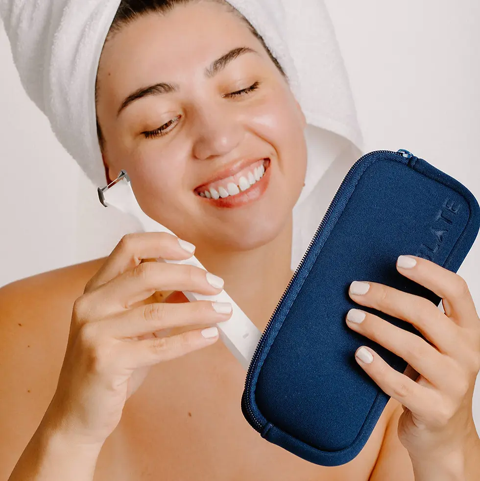 Smiling woman with a towel on her head holds a white beauty tool and a blue case. White background, relaxed mood.