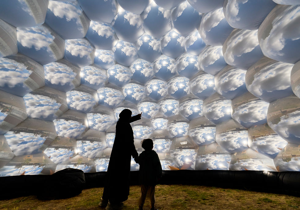 Silhouetted adult and child inside a cloud-printed inflatable dome, with the adult pointing upward under a bright sky scene