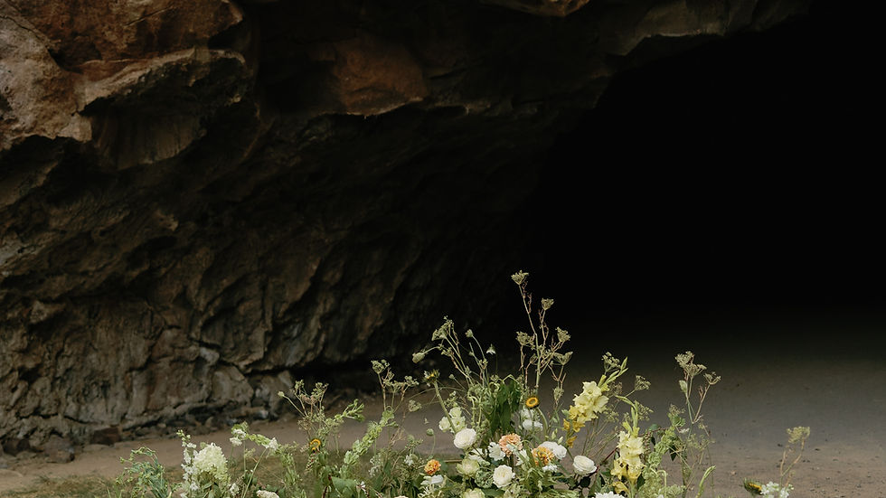 Floral arrangement with white and yellow flowers on sandy ground in front of a rocky cave entrance. Natural, serene atmosphere. Dreamy Green and White Flowers Inspirations