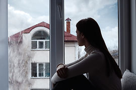 Photograph showing a woman sitting beside a glass window and looking outside.