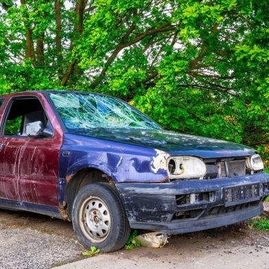 Une épave de voiture abandonnée avec des vitres brisées au bord du parking